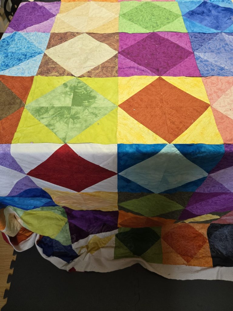 A colorful patchwork quilt with diamond and square patterns in various bright and neutral colors draped over a surface.
