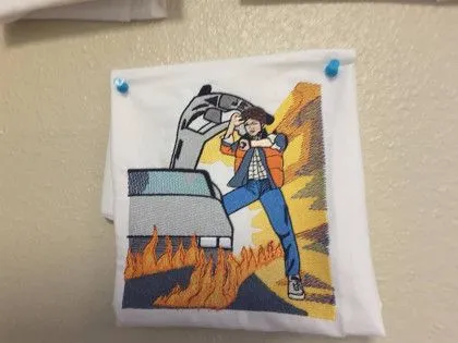 Embroidered patch of a person posing in front of a car with flames and an explosion in the background.
