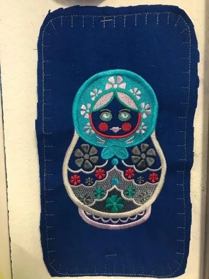 Embroidered matryoshka doll design on a rectangular piece of dark blue fabric.