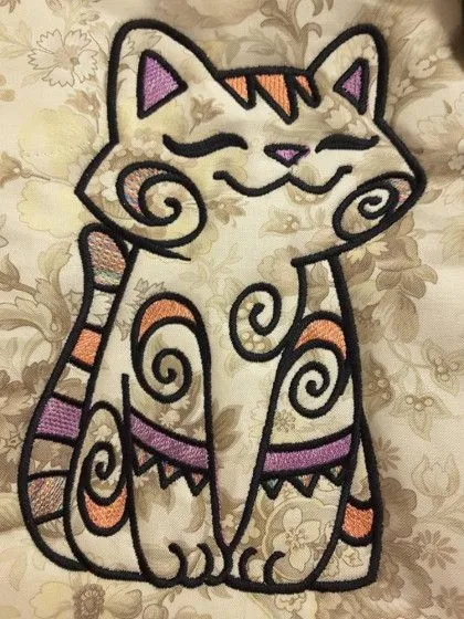 Embroidered cat with swirled patterns and pastel colors on a floral fabric background.