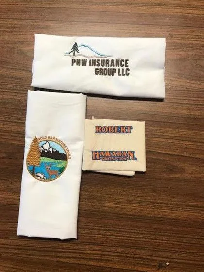 Four folded white fabric items with different business logos and names, laid out on a wooden surface.