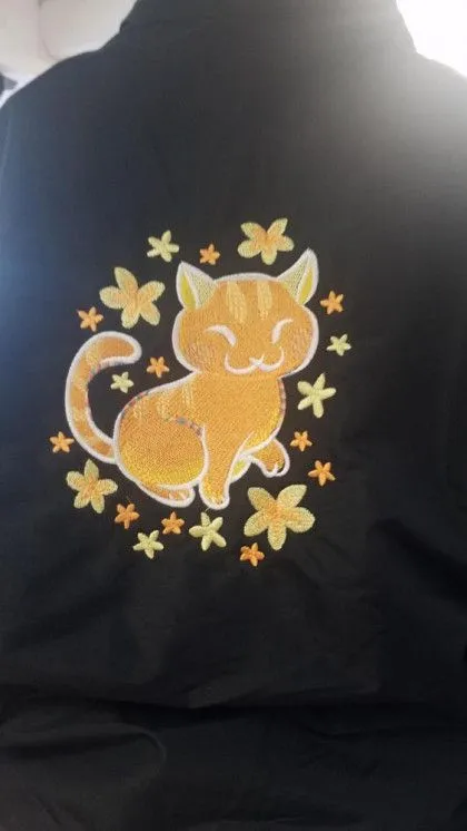 Embroidered orange cartoon cat surrounded by yellow and orange flowers on a black fabric background.