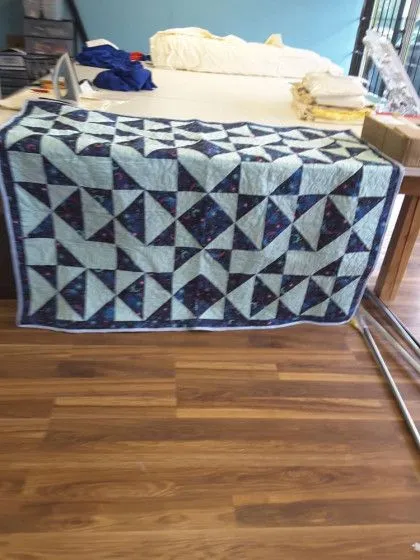 A handmade quilt with a geometric triangle pattern in blue tones draped over a table in a room with wooden flooring.
