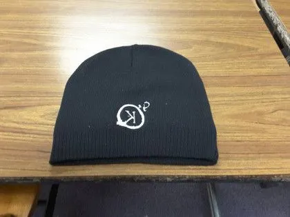 A black beanie with a white embroidered "OK" symbol sits on a wooden desk.