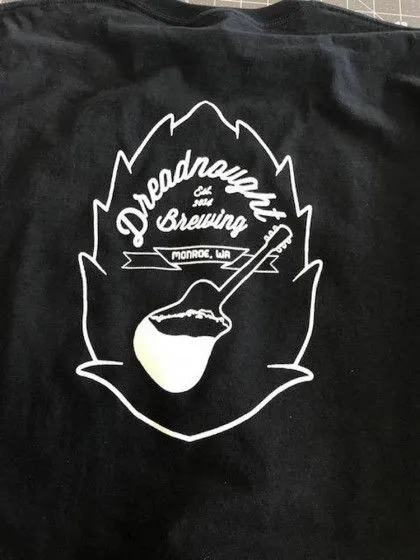 Black t-shirt with a white "Dreadnought Brewing Monroe, WA" logo featuring a hop outline and a mash paddle.