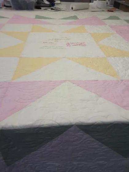 A pastel geometric quilt with star patterns is spread out on a table in a workspace.