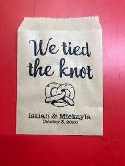 A brown paper bag with "We tied the knot" and pretzel graphic, plus names Isaiah & Miekayla, October 3, 2020.