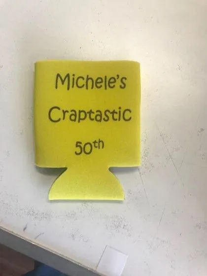 A yellow drink koozie with the words "Michele's Craptastic 50th" printed on it.