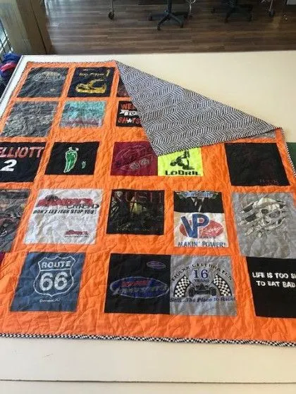 A quilt made from various colorful t-shirts with an orange border and a black and white patterned backing.