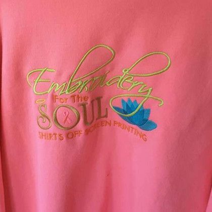 Pink shirt with yellow-green embroidered text "Embroidery For The Soul" and blue flower graphic underneath.