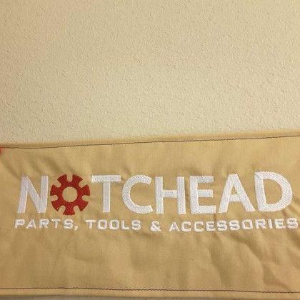 Tan fabric with embroidered text reading "NOTCHEAD PARTS, TOOLS & ACCESSORIES" and a red gear in place of the "O".