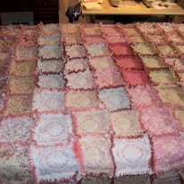 A patchwork quilt made of square fabric pieces in shades of pink, cream, and beige is spread out on a table.
